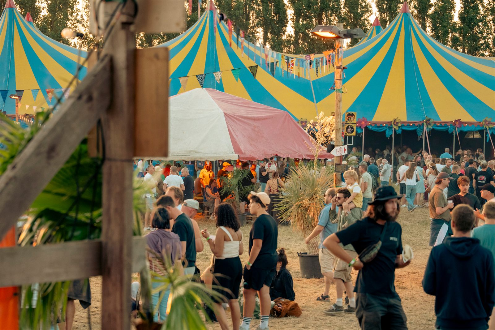Regenboogkleurige circustenten boven een druk festivalterrein