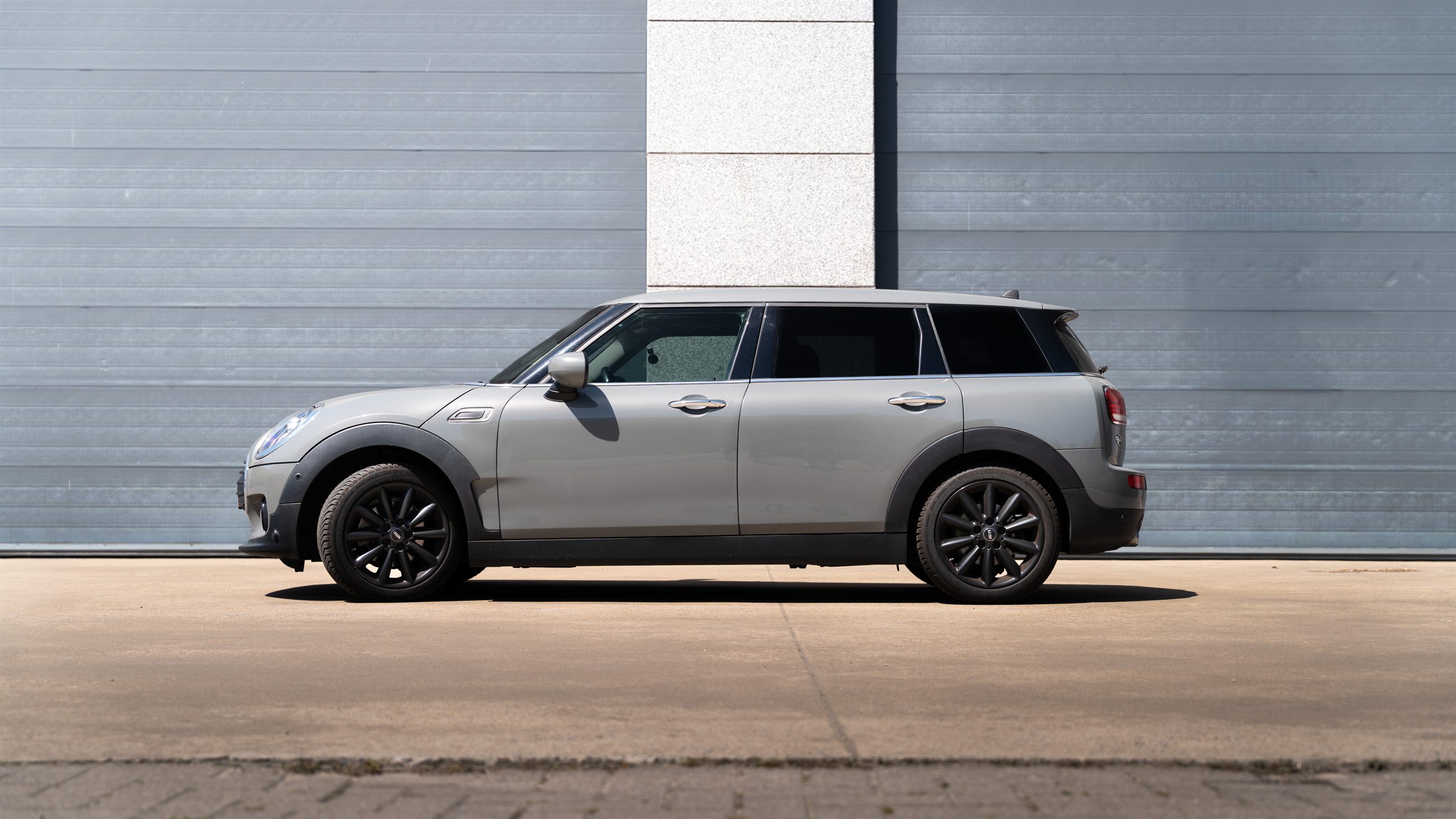 Grijze MINI Clubman van opzij voor een metalen gevel